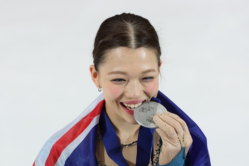 Hana Bath bites a silver medal as she holds it to her mouth while wrapped in an Australian flag