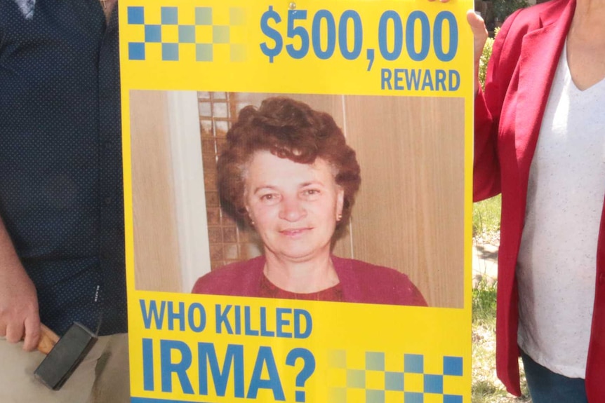 John and Liz stand holding a sign promising a $500,000 reward for helping identify the killers.