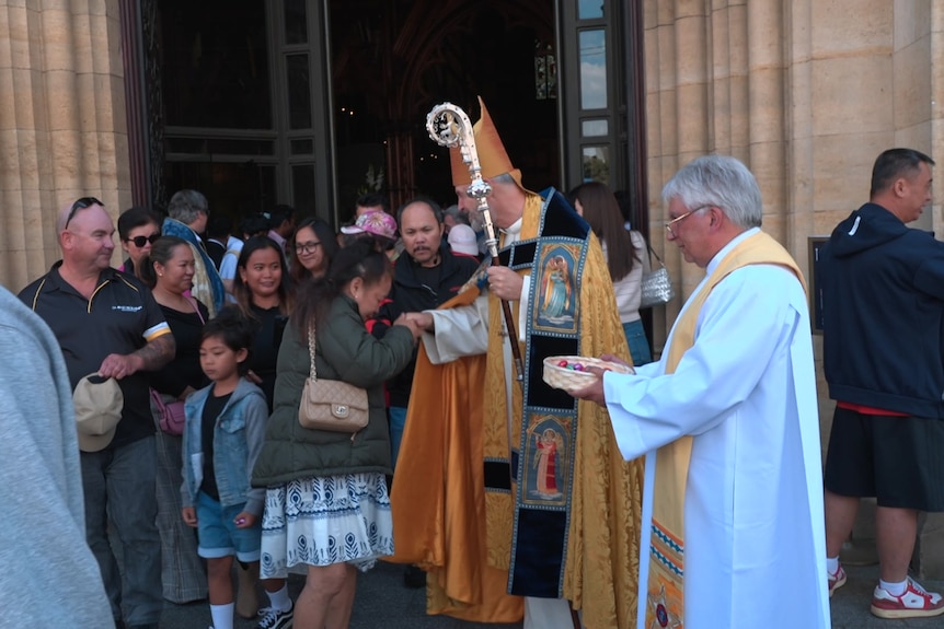 An archbishop shaking hands with people outside a cathedral