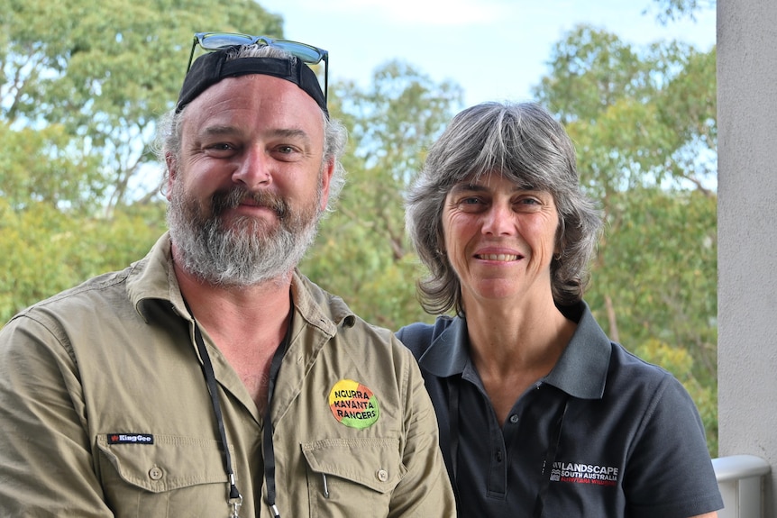 A man and a woman standing together with gum trees in the background