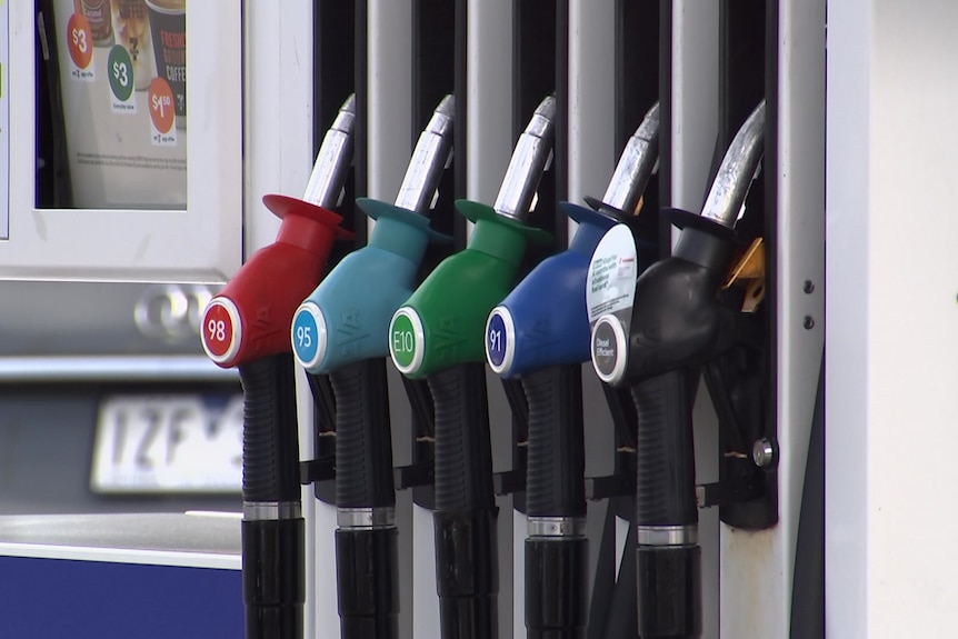 Five red petrol pumps in a bowser; one with a red handle, then a blue, a green, a dark blue and a black handle.
