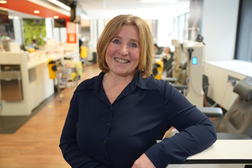 A woman smiles while leaning an arm on a countertop in front of several chairs and plasma machines.
