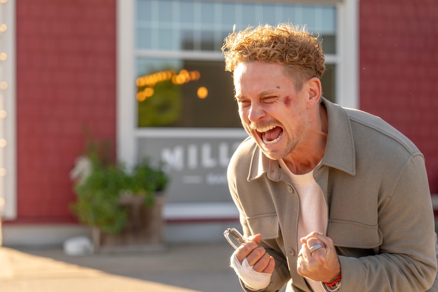 A man screams in front of a red building.