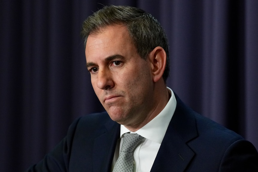 A man with short, dark hair, wearing a suit jacket and tie, looking serious.