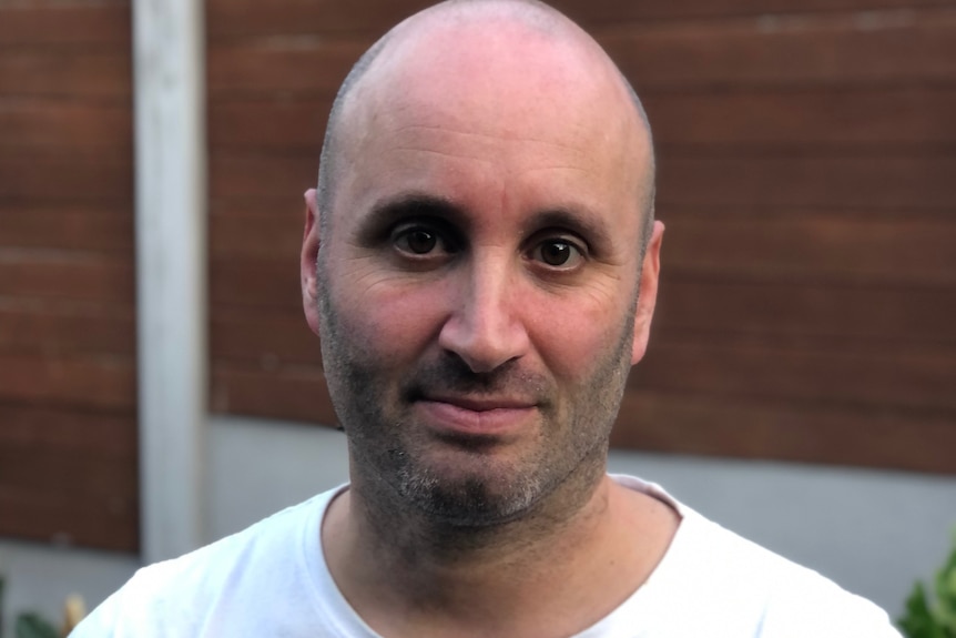 A man wearing a white tshirt looks to camera.