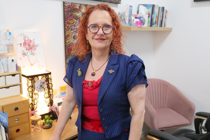A woman with curly hair inside her office, with paintings and chairs in the background