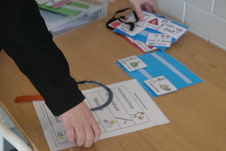 A wooden desk with laminated children's activities laid out on it and a woman's hand reaching out for some of the paper.