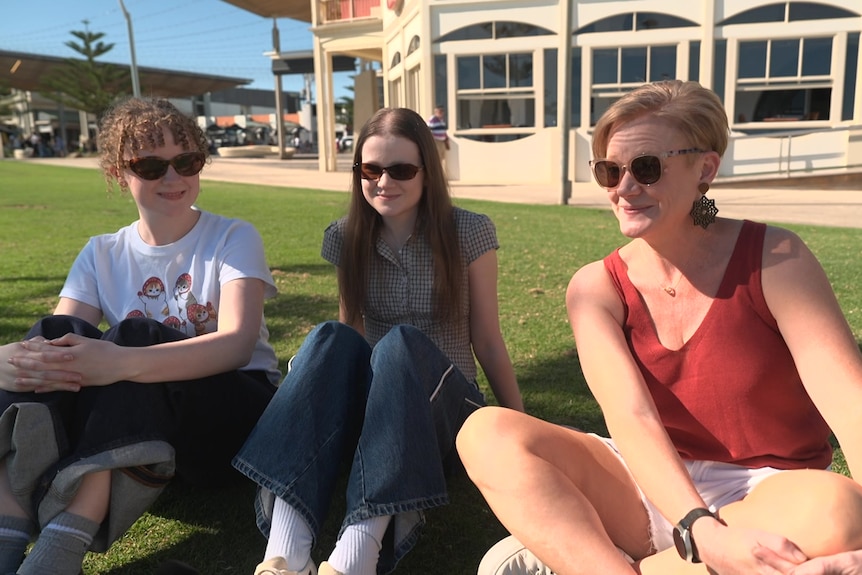 Three women sitting on grass outside a building