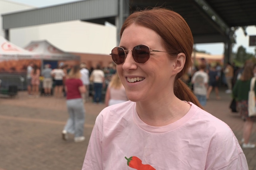 A woman in sunglasses smiles in front of many attendees at an outdoor market