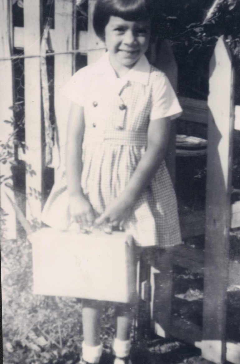 A young girl holding a suitcase smiles at the camera. 