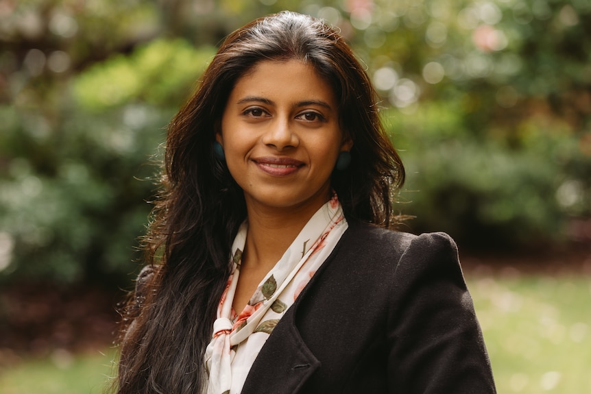 Dr Ali Saha poses in front of a green, tree background