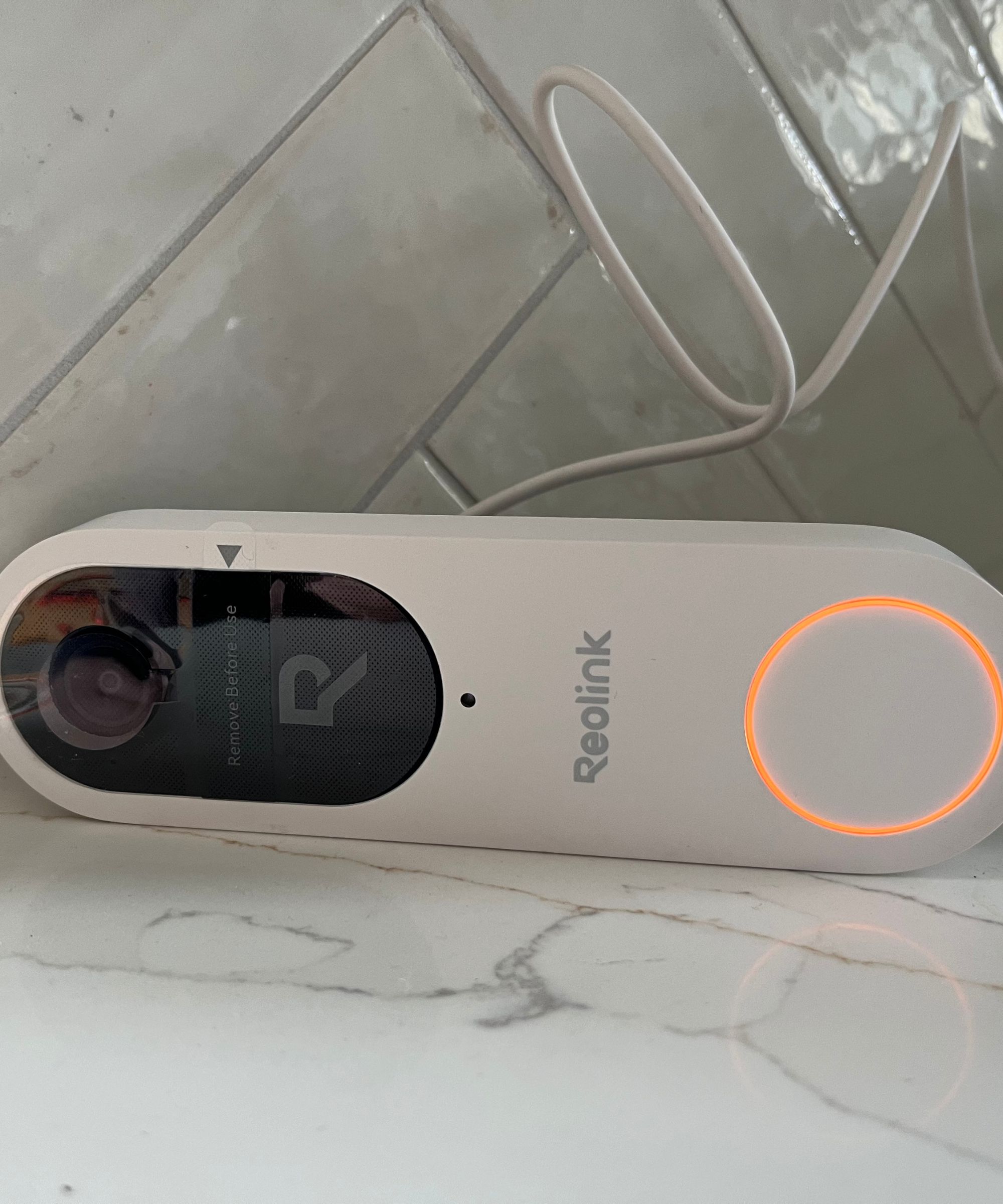 Reolink video doorbell (battery) plugged in and charging, displaying orange charger light.