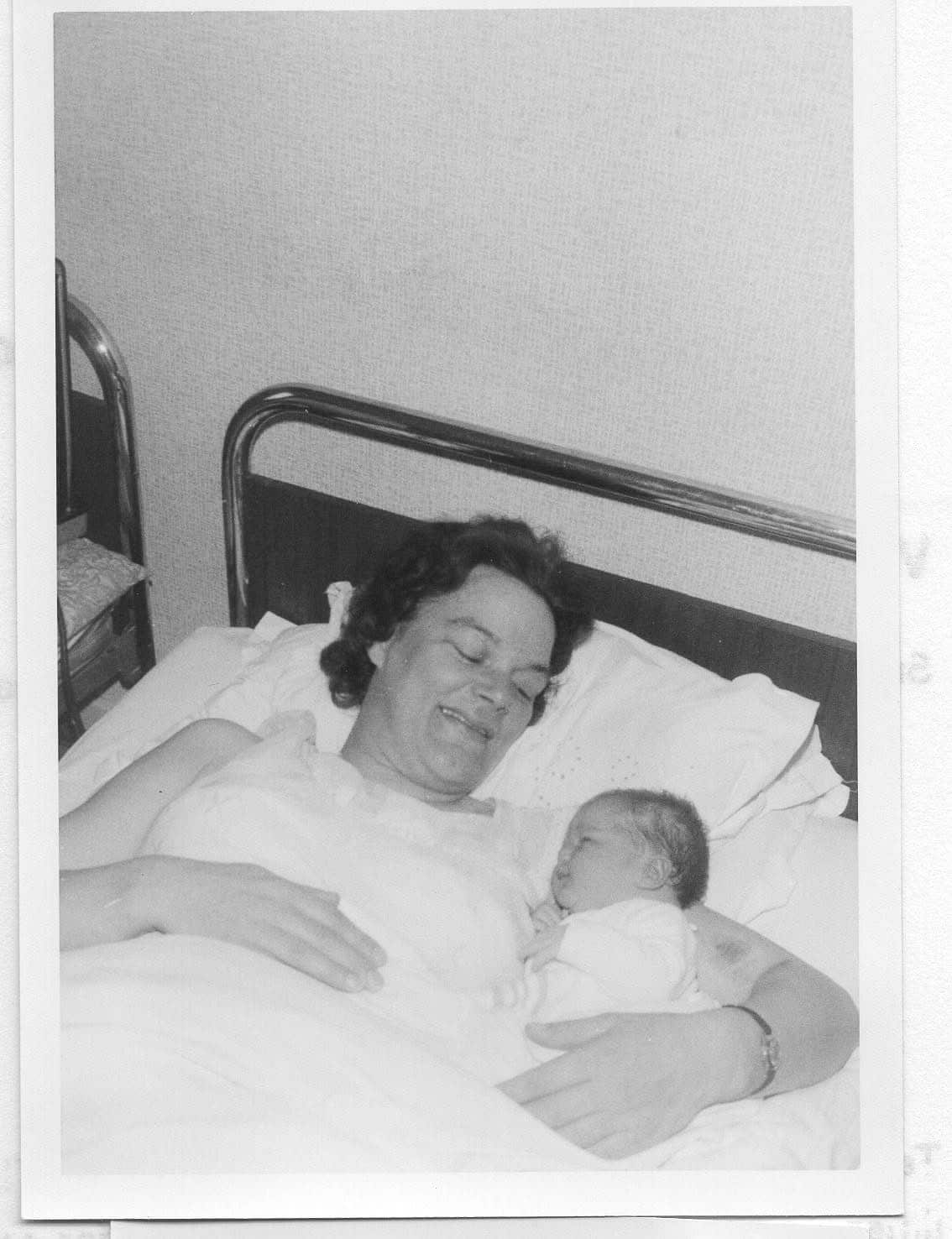 A black and white photo of a mother lying in bed, snuggled up to her newborn baby. 