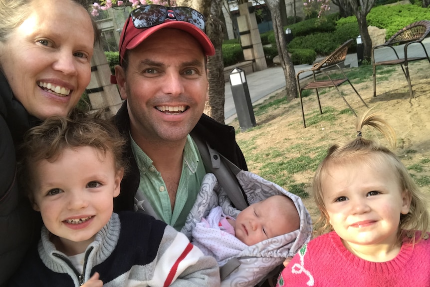 Woman and man holding a baby, with a young boy and girl smiling at camera
