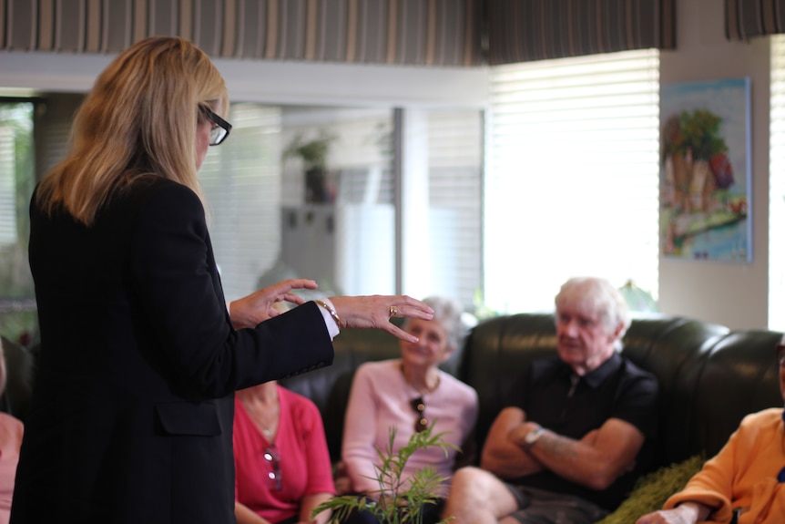 A woman talking to a group of older people sitting in a living room