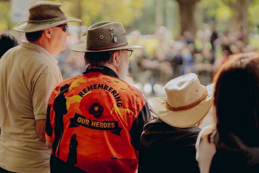 Man wearing an Indigenous shirt with the words Remembering our heroes at sydney anzac day service 