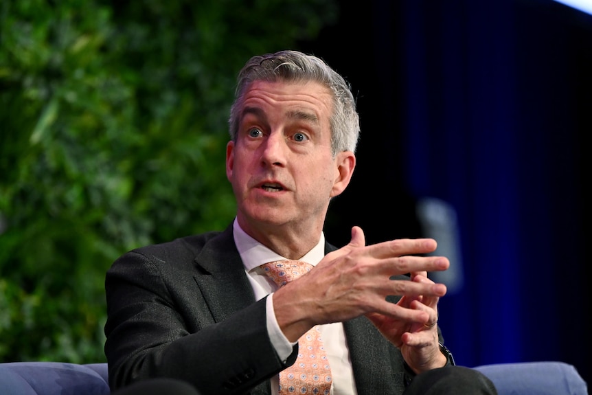 A man wearing a suit and tie gestures with his hands while speaking.