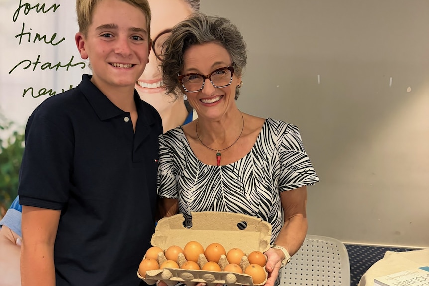 A teenage boy and woman stand with a carton of eggs.