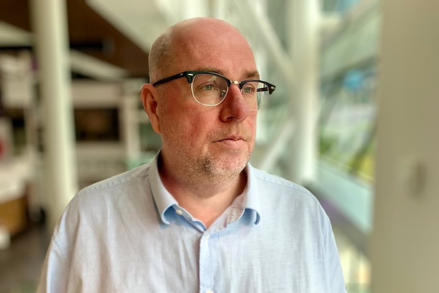A man in glasses and a blue shirt looks to the right of the camera.