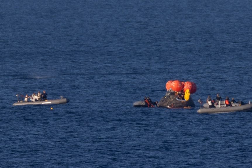 A zoomed-in picture of two rescue boats approaching a spacecraft landed in the sea