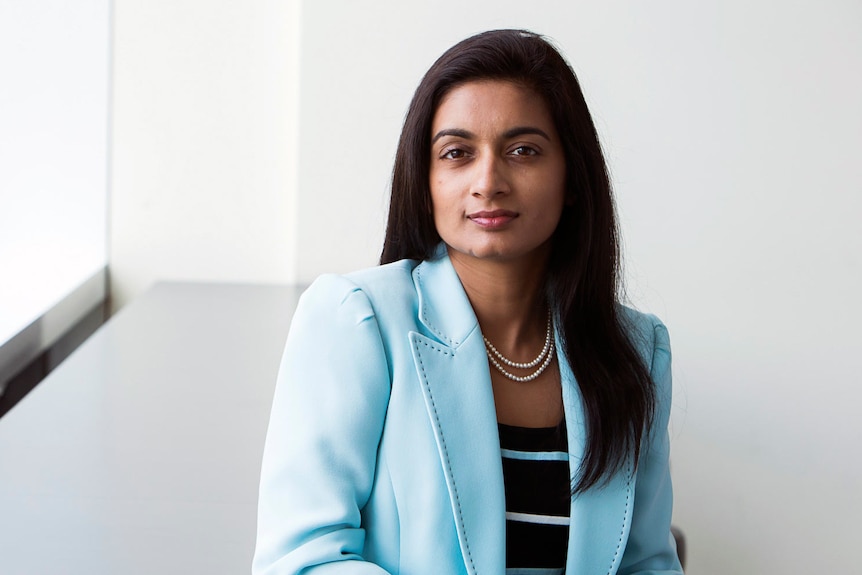 Woman with long hair over one shoulder, wearing a light blue jacket, looking at the camera