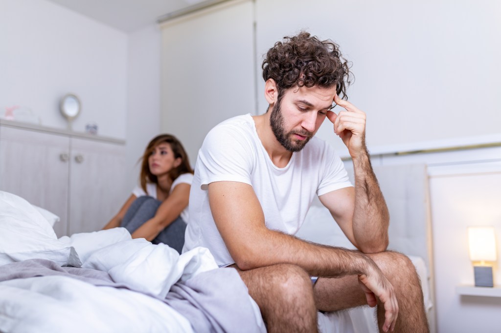 A frustrated man and woman sitting in bed, ignoring each other after a fight.