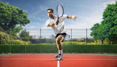 Male tennis player in action, hitting a forehand on an outdoor court, dynamic sports shot with racket motion, fenced court surrounded by greenery and city skyline in the background.