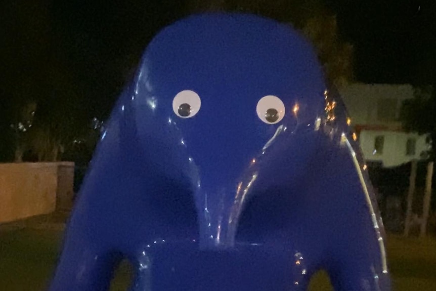 A large blue sculpture with googly eyes on it at night.