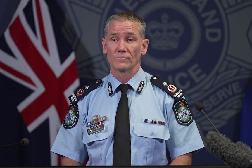 A police officer in uniform speaking at a press conference in front of police logo and flag.