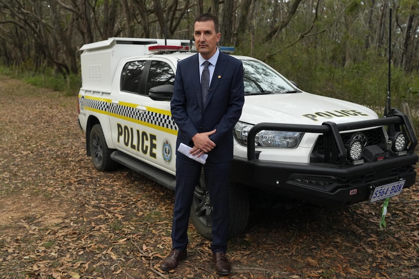 A man wearing a suit and tie stands next to a police wagon