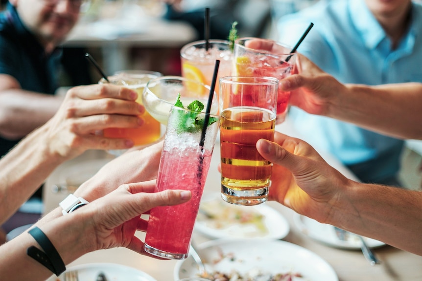 A group of hands holding up cocktails for a toast.