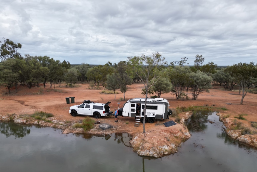 A car with a caravan on the back next to a river in the outback, photo taken high up for birds eye view