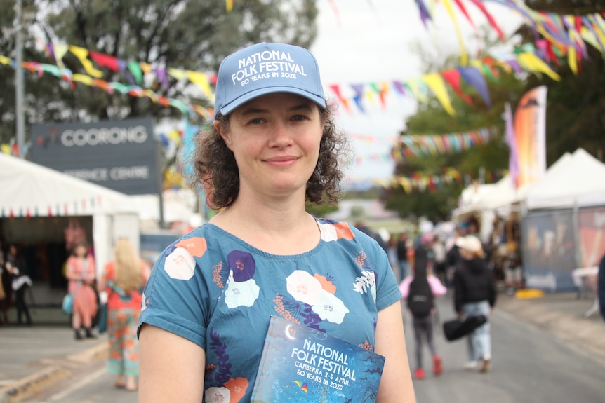 A woman wearing a National Folk Festival cap and holding a booklet.