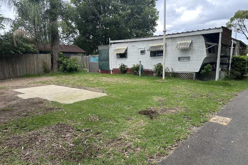 An empty lot with a small concrete slab, next to a caravan under a permanent awning.