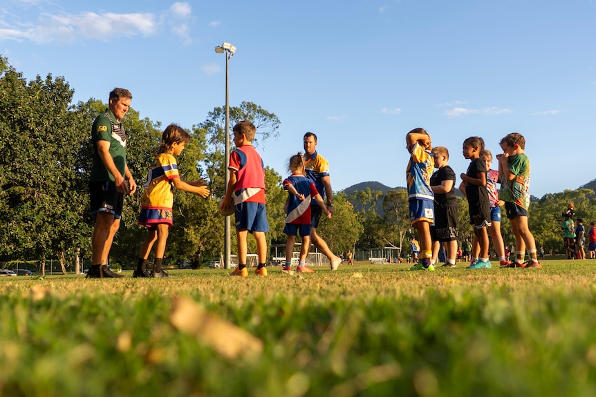A group of children stand on a football field passing a ball in the afternoon light.