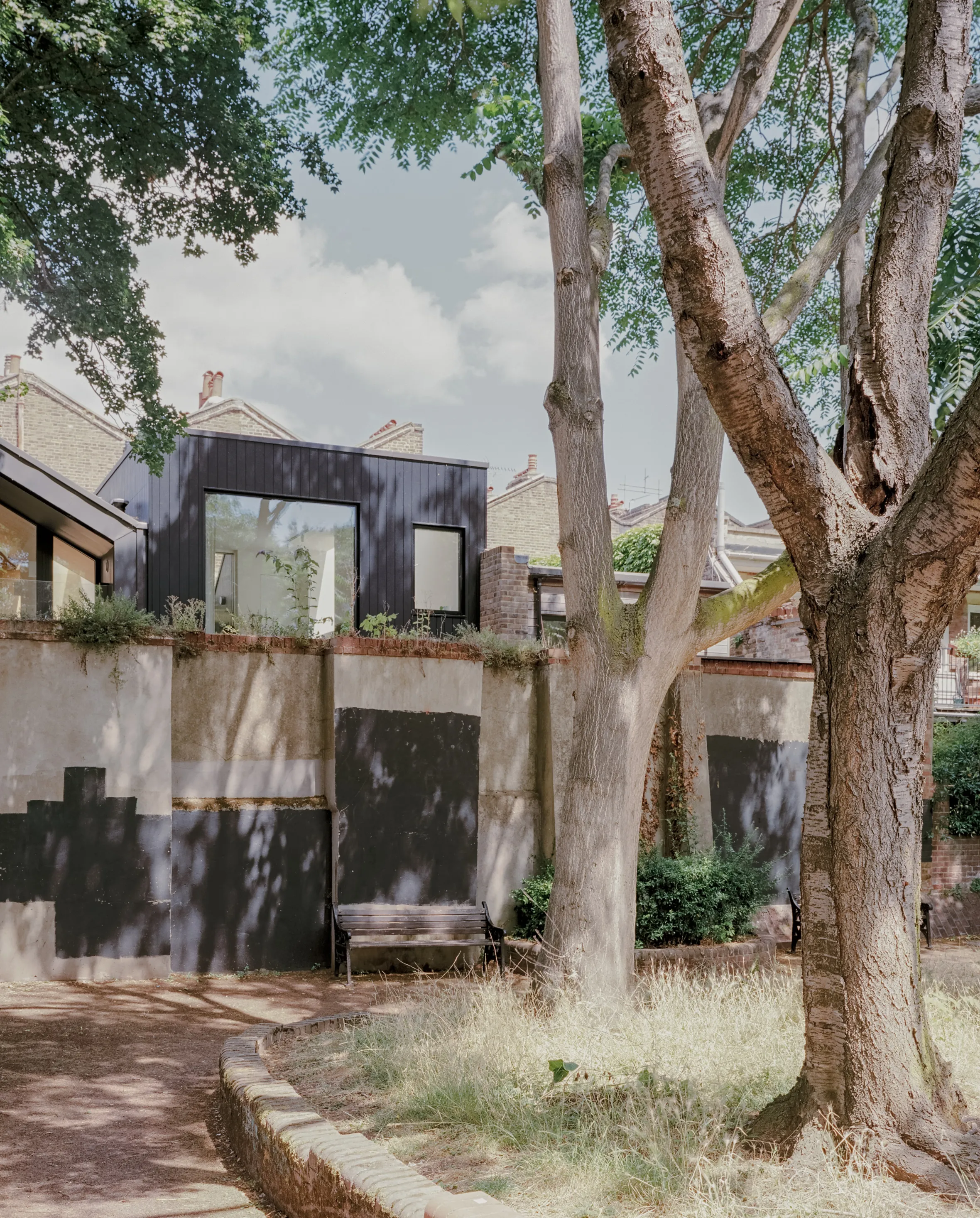 Greenview House's black exterior and large windows, as seen from a garden with two large trees and a low wall.