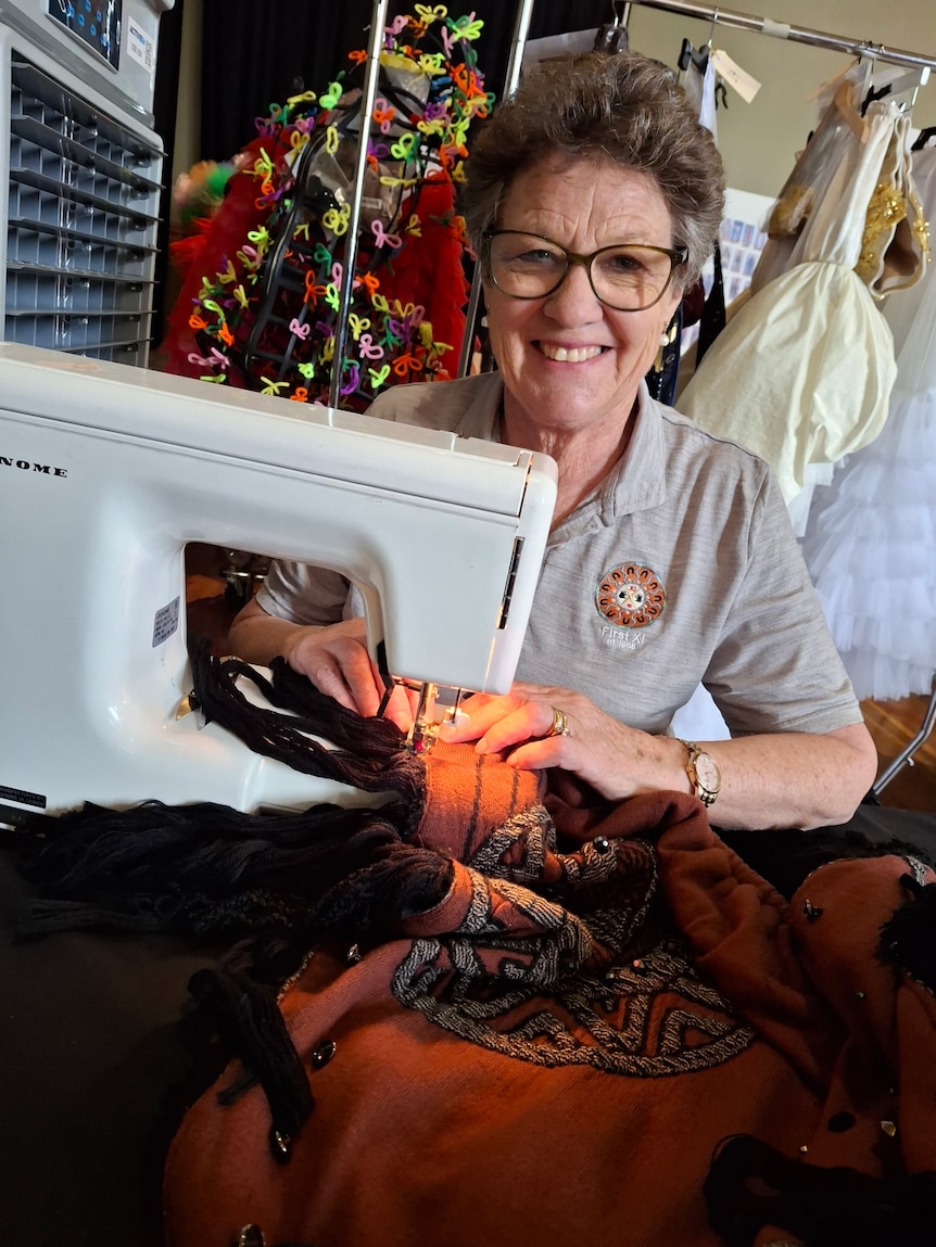Elderly woman sewing red material with white sewing machine, smiling