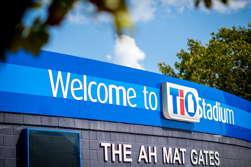 A sign reading 'Welcome to TIO Stadium' on the top of a wall surrounding a stadium.