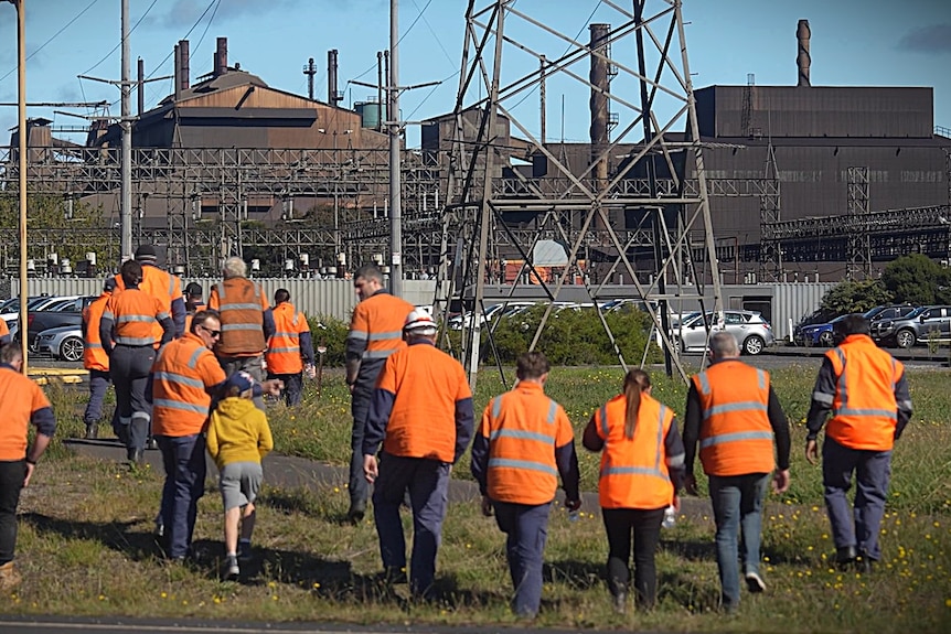 Workers walking towards an industrial smelter.
