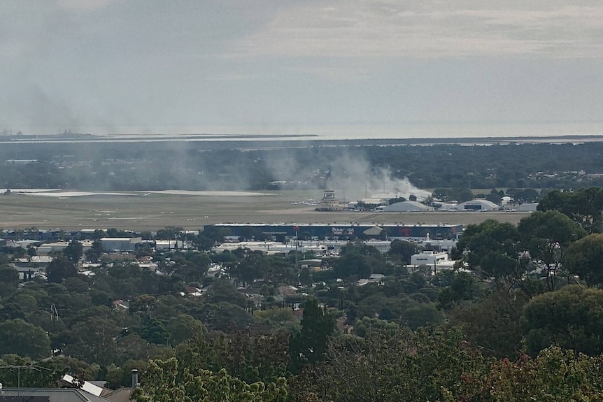 White smoke comes from an airport with a suburban street in the foreground