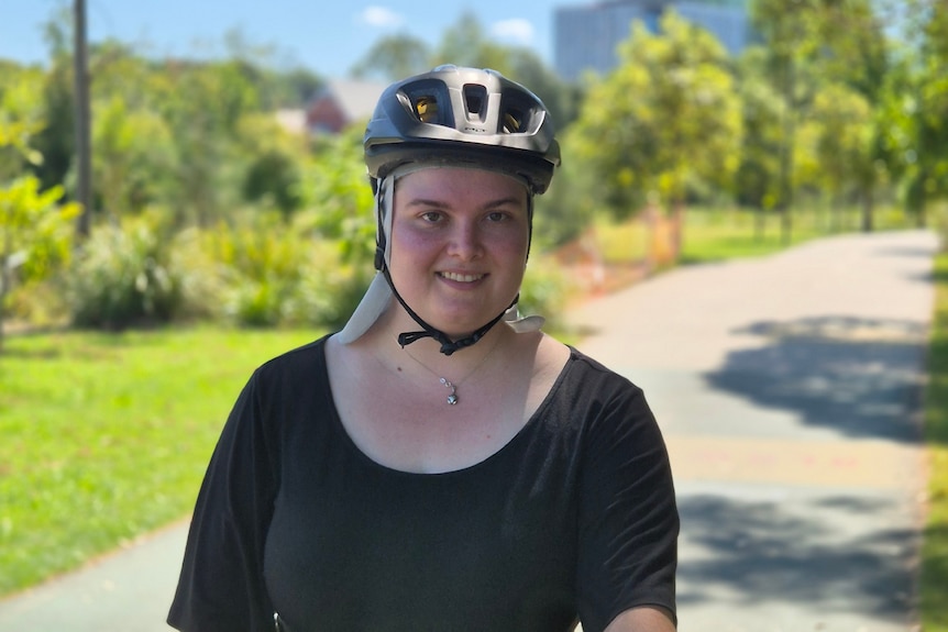 A woman in a black top and helmet on a bike path and on a bike