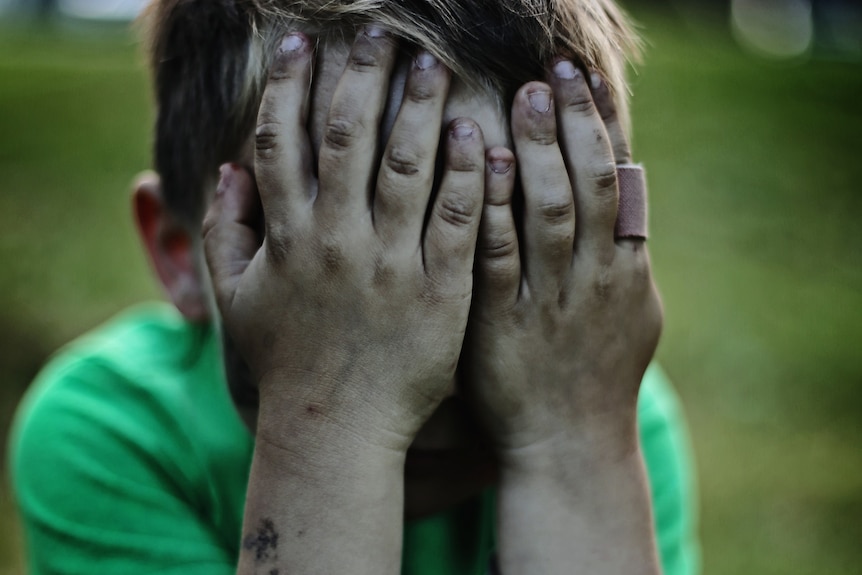 A small boy covering his face with both hands while throwing a tantrum.