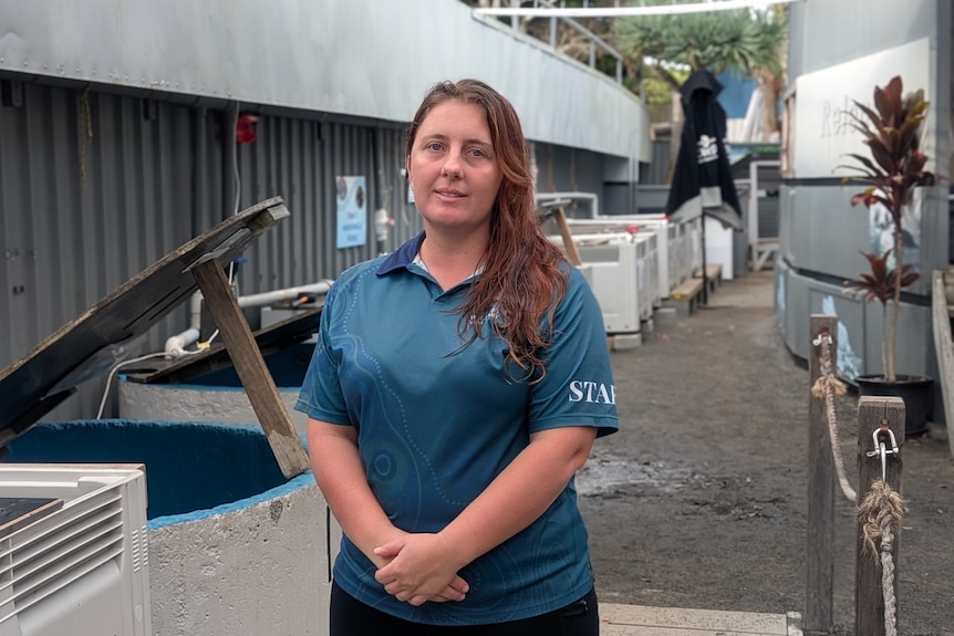 A woman in a blue shirt, with long brown hair, stands at a wildlife sanctuary.