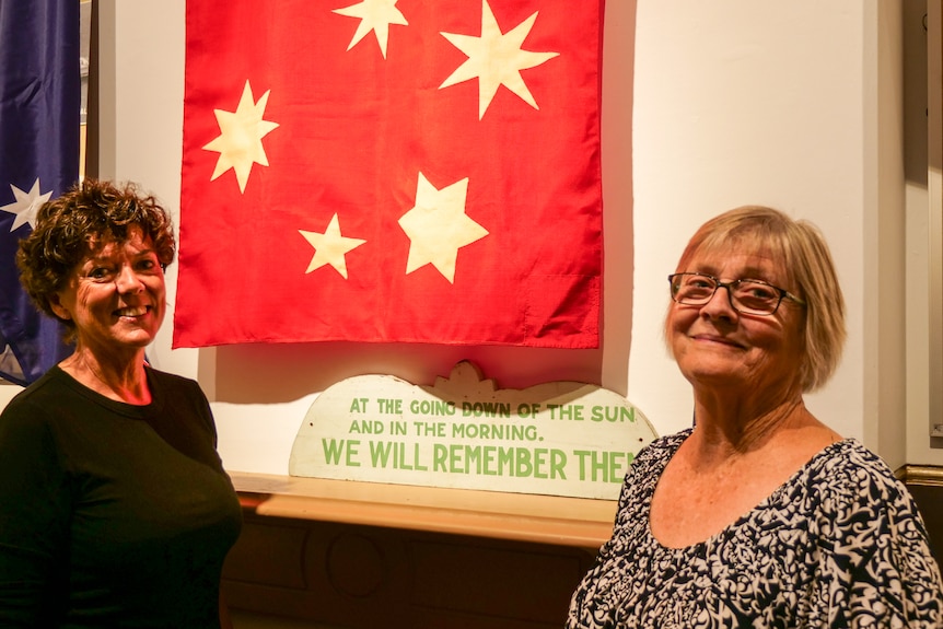 Two women stand in front of a newly restored flag.