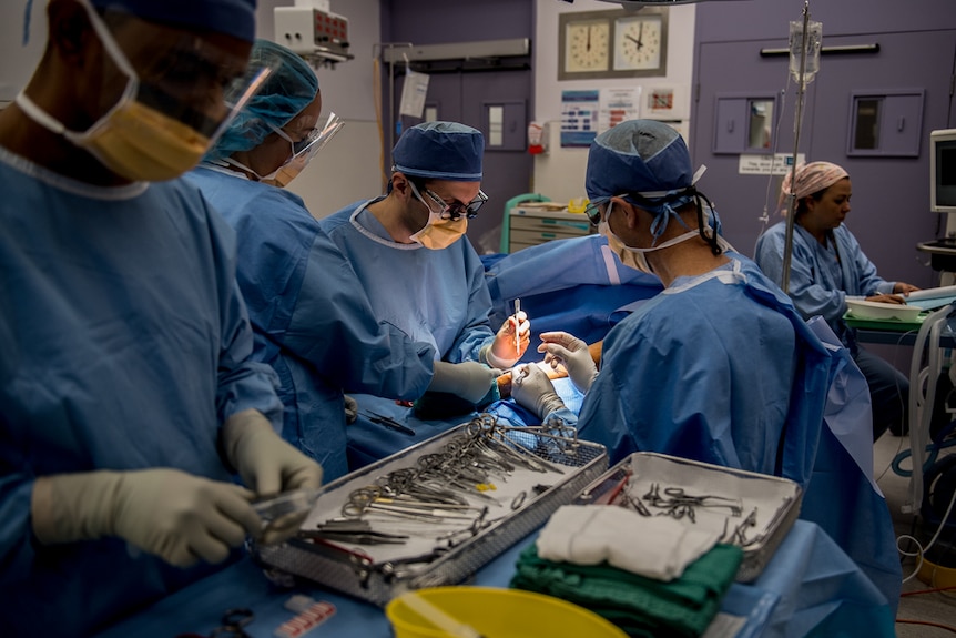 A photo of people operating on a person in theatre, all in blue.