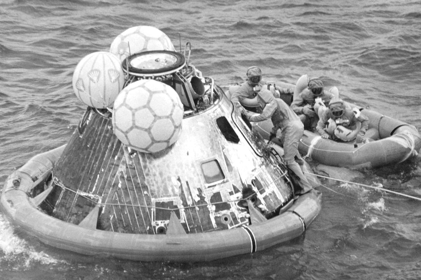 Navy sailors collect the Apollo 11 astronauts from their space capsule floating in the ocean and take them onboard a dinghy.