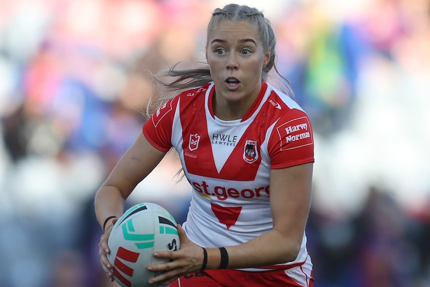 A St George Illawarra NRLW player runs with the ball in two hands during a match.