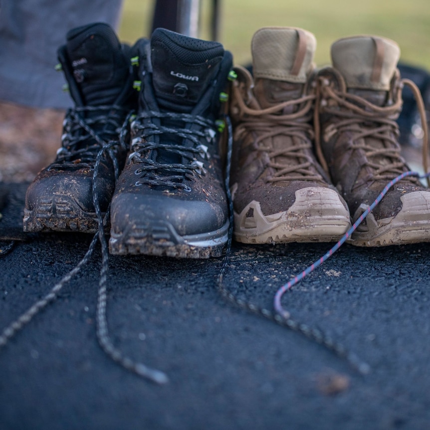 Three sets of dirty boots lined up on the ground