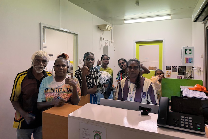 A group of people in varied ages standing behind a counter, some with thumbs up