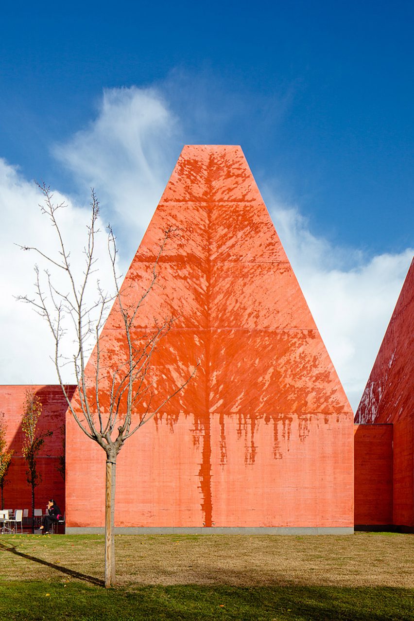 Exterior view of a pyramidal tower showing weathering patterns on the red concrete surface